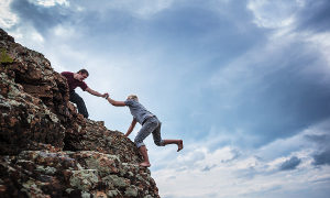 Man giving helping hand to friend to climb mountain rock cliff